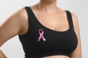 Caucasian unrecognizable woman in a black seamless bra with a pink ribbon for breast cancer. Studio anonymous photo image medium shot on white background.