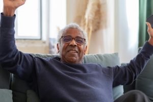 homem negro idoso de óculos e sueter azul comemorando ganho em jogo online com celular na mão